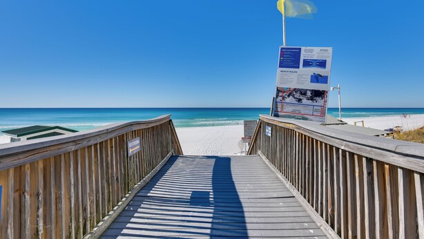 Una passerella di legno che conduce a una spiaggia, con cielo sereno e una bandiera.