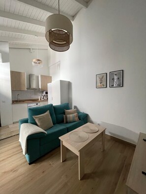 Ett modernt vardagsrum med en turkos soffa, ett soffbord i trä och en hängande lampa.