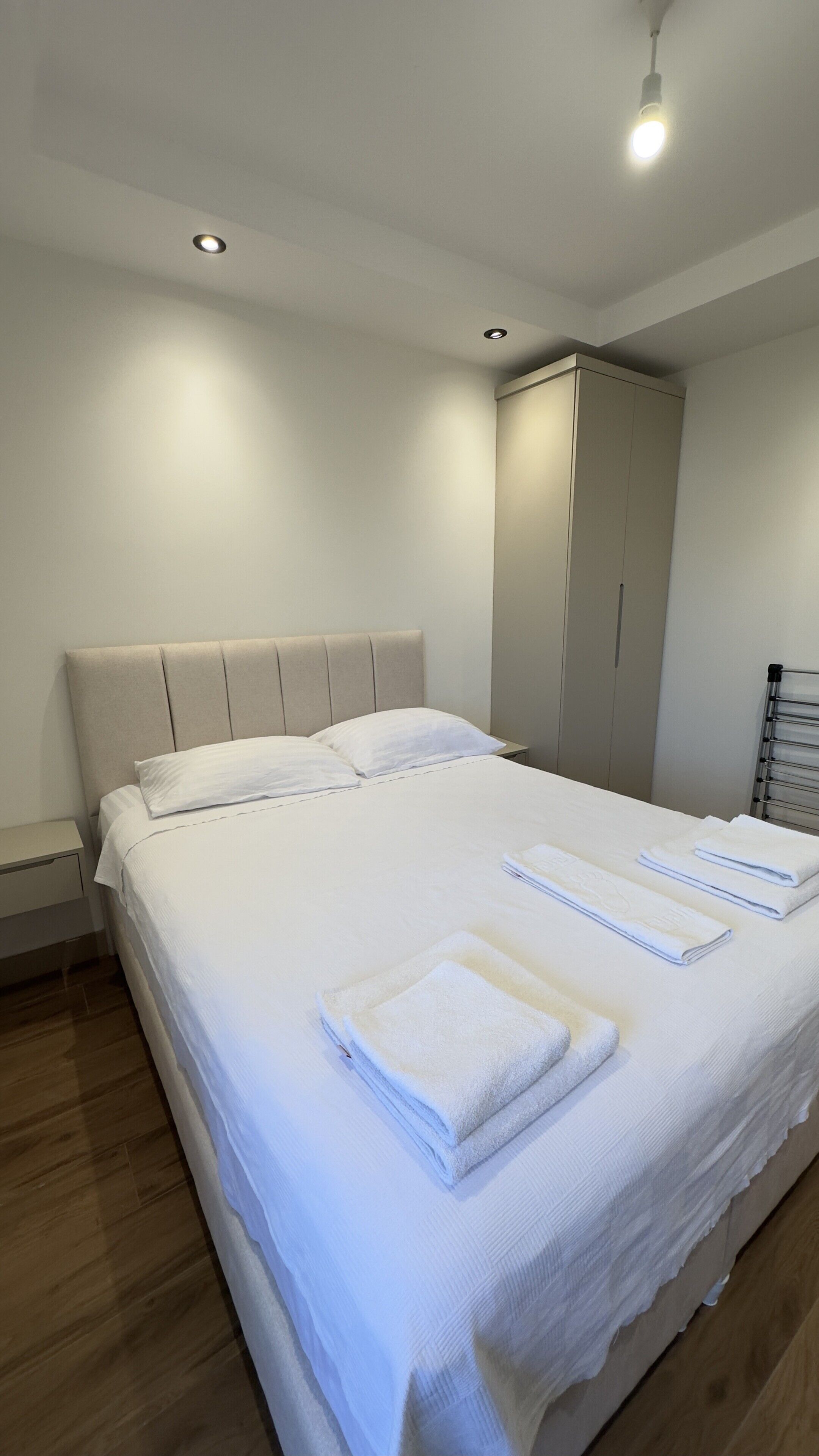 Una cama bien hecha con ropa de cama y toallas blancas, una mesita de noche y un armario en una habitación de hotel.