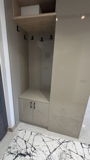 A walk-in closet with a marble-patterned floor, a wooden shelf, and a hanging rod. - NestParkSide (Manavgat)