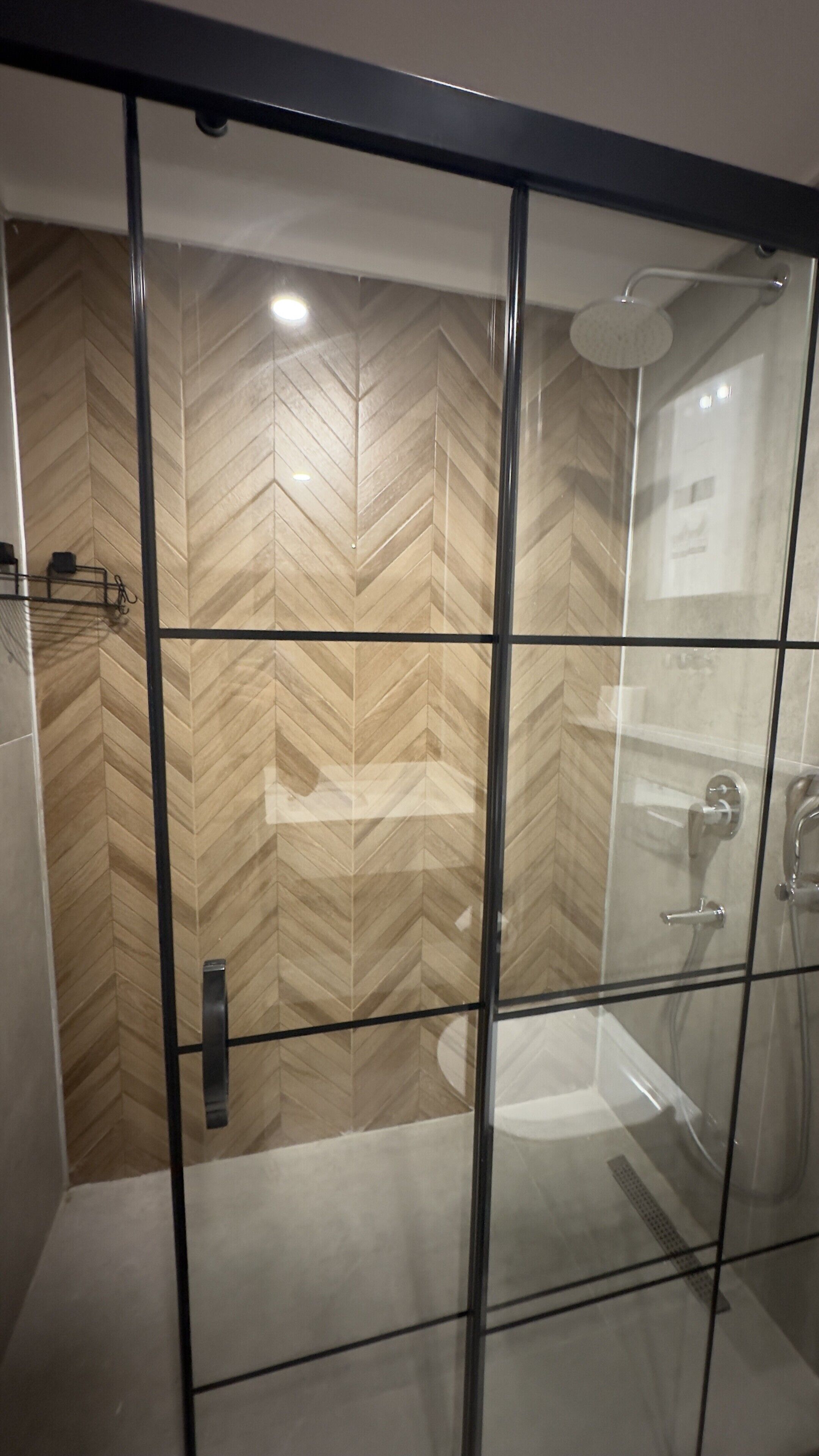 Un baño moderno con cabina de ducha de vidrio, pared con patrón de espiga y ducha a la vista.