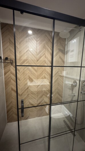 Casa de banho moderna com cabine de duche em vidro, parede com padrão herringbone e chuveiro à mostra.