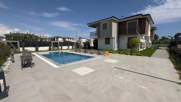 Un quartier résidentiel doté d’une piscine, de chaises longues et d’une maison moderne à deux étages.