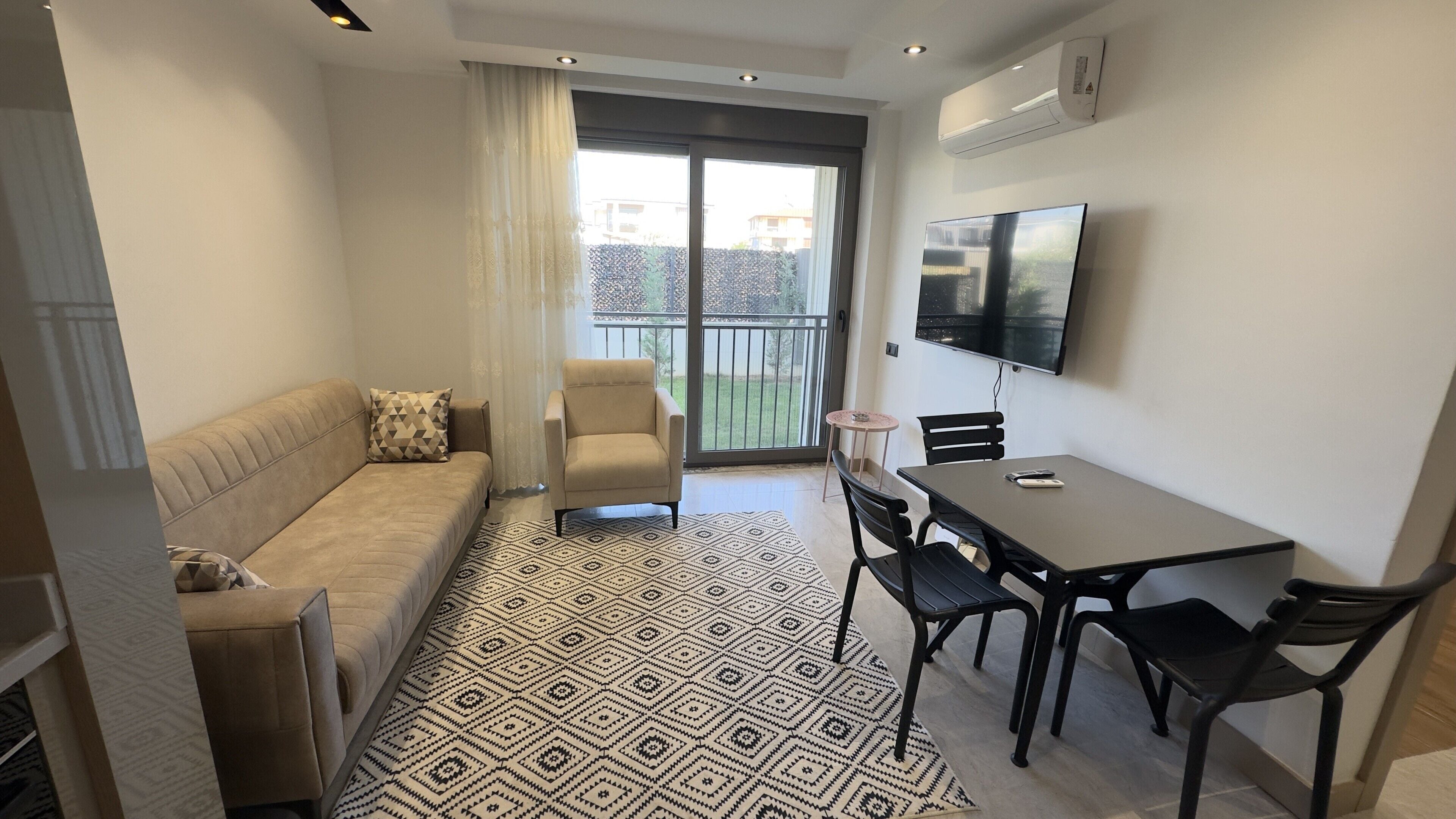 Ein modernes Wohnzimmer mit einer Couch, einem Esstisch mit Stühlen, einem an der Wand befestigten Fernseher und einem Balkon mit Blick.