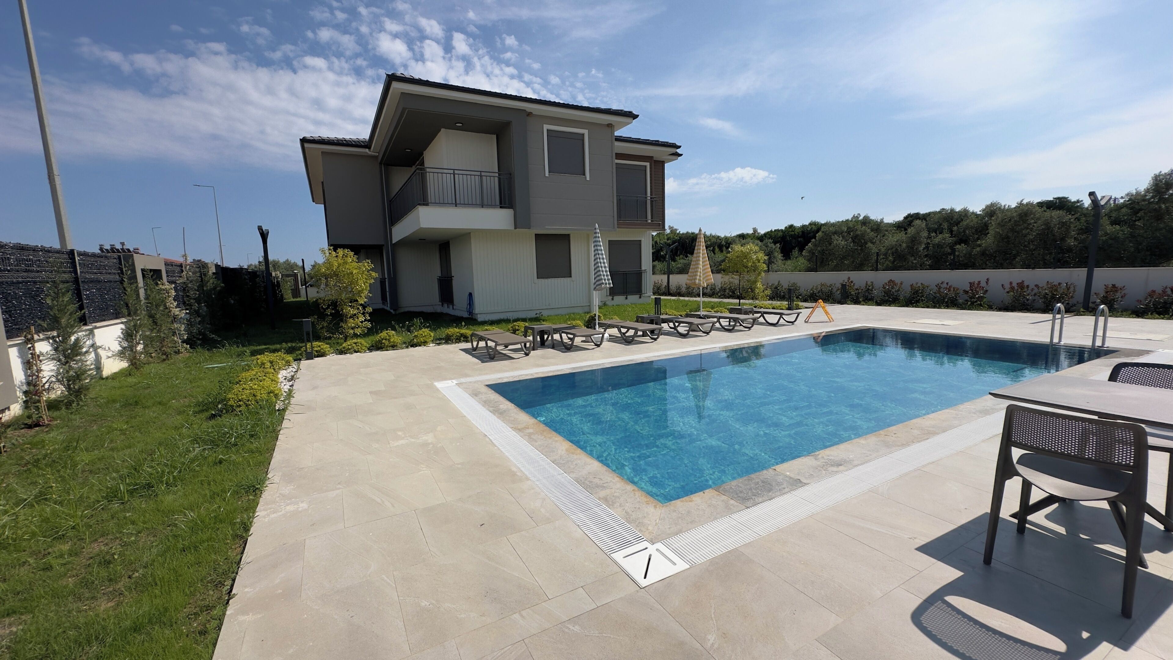 Una casa moderna de dos pisos con piscina, mobiliario exterior y jardín cuidado.