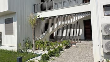 Ein modernes Gebäude mit weißer Fassade, einer Schotterauffahrt und einer Treppe, die zu einem Balkon führt.