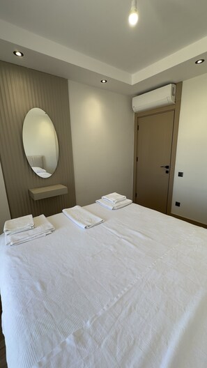Una habitación de hotel con una cama grande, un espejo, una mesita de noche y un equipo de aire acondicionado.
