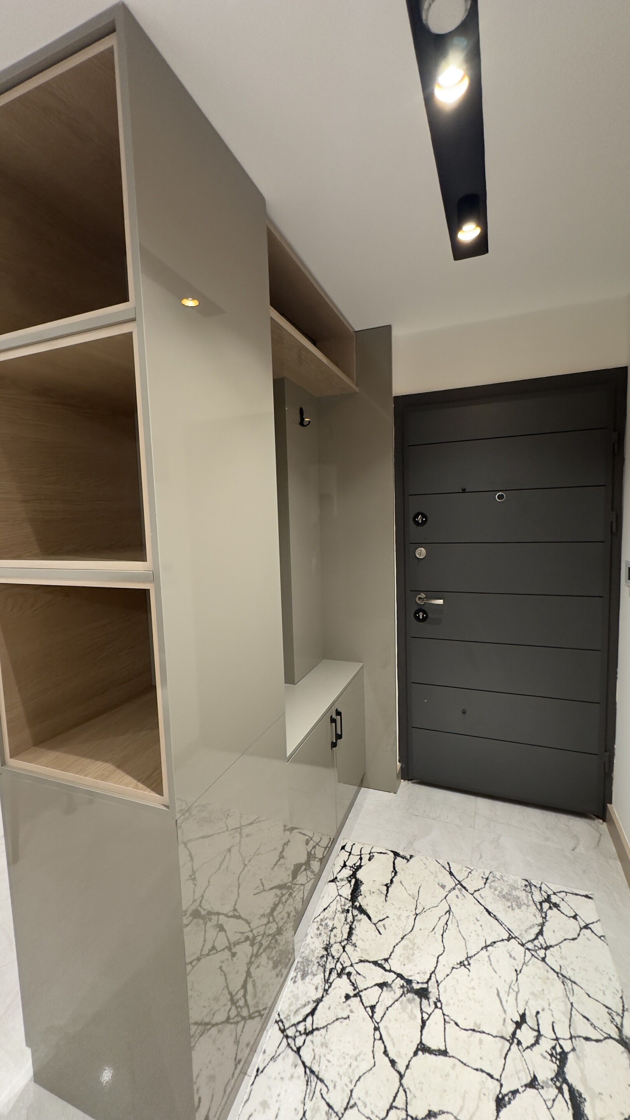 Una habitación con una puerta oscura, suelo de mármol blanco y estanterías empotradas.