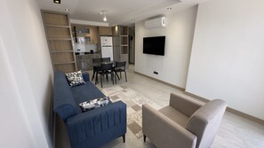 Un salon moderne comprenant un canapé, un fauteuil, une table à manger avec des chaises, ainsi qu’un coin cuisine avec des placards et un réfrigérateur.