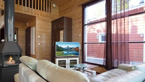 Een gezellig chalet interieur met een open haard, een bank, een televisie en een groot raam met gordijnen.