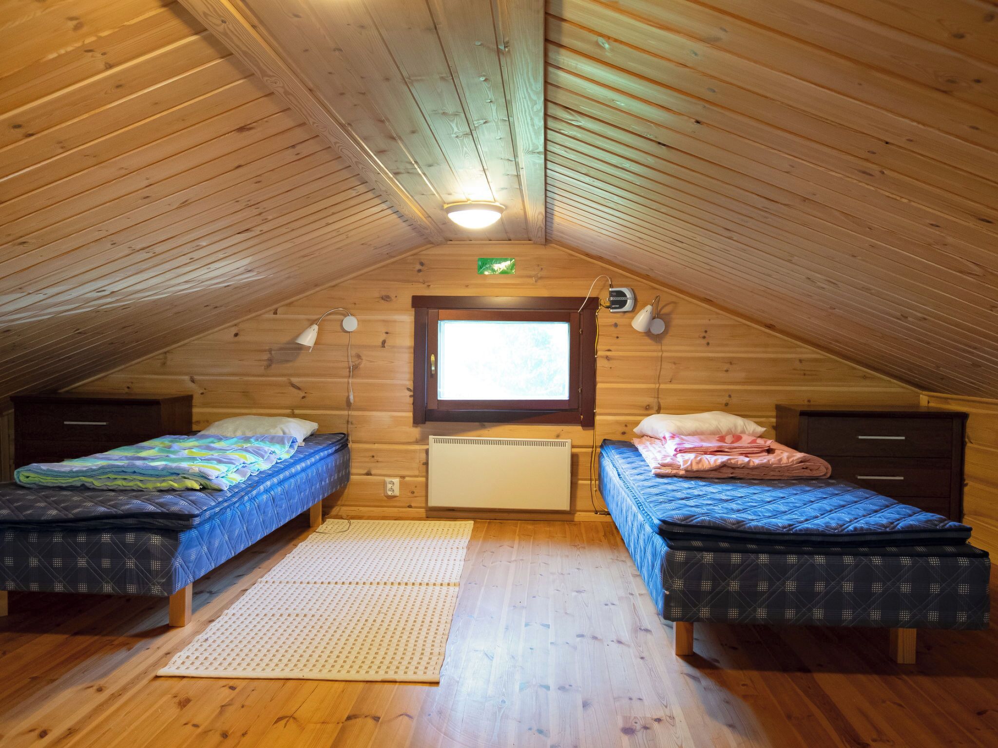 A cozy attic bedroom with two beds, a window, a heater, and a lamp.