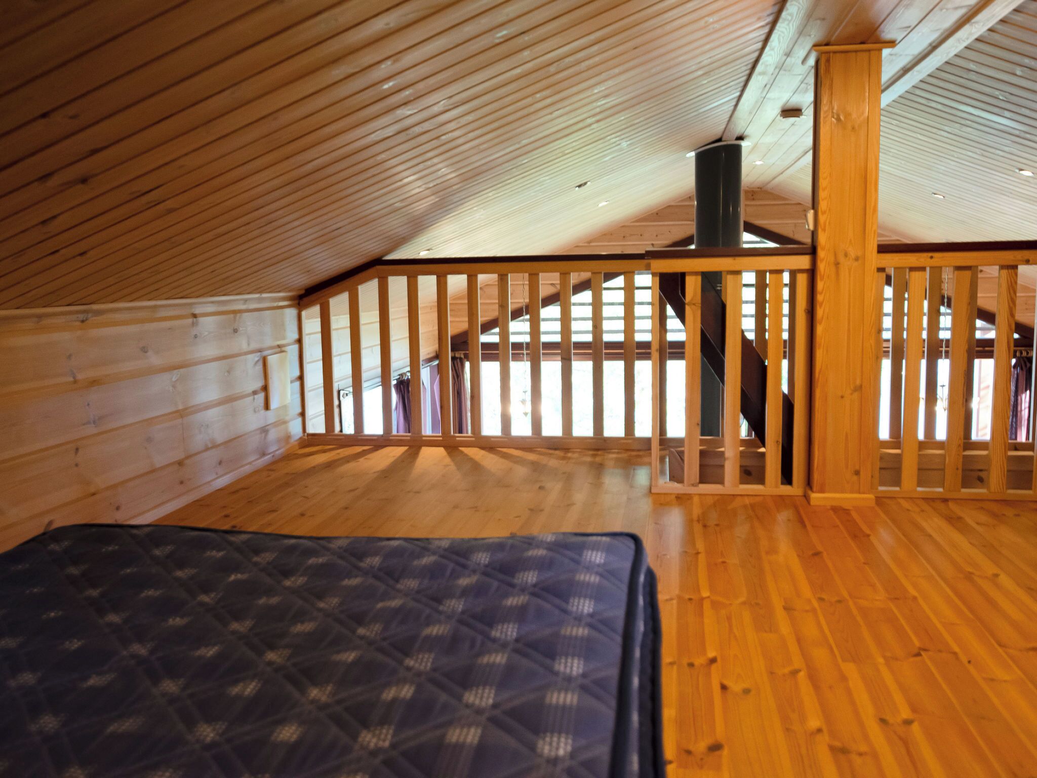 Une chambre située dans un espace de type « loft », avec un plafond en pente en bois, un lit et un escalier menant à un niveau supérieur.