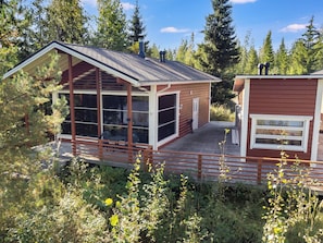 Une cabane dotée d’une grande fenêtre en verre, d’une terrasse et d’une cheminée.