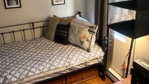 Ein Schlafzimmer mit Bett, Holzkasten, Regaleinheit und gerahmten Bildern an der Wand.