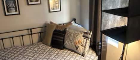 A bedroom with a bed, wooden drawers, a shelf unit, and framed pictures on the wall.