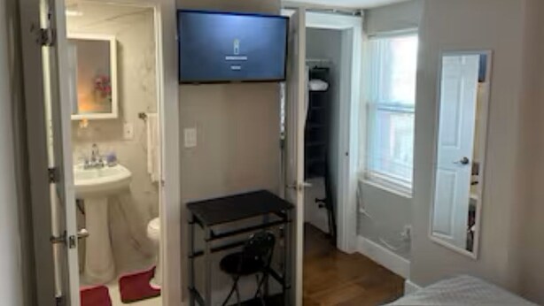 Ein Zimmer mit Bett, Schreibtisch, Stuhl, Fernseher und einem durchgegangenen Tür sichtbaren Badezimmer.