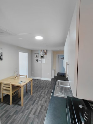 A modern kitchen with a wooden dining table, grey flooring, and a stainless steel sink. - Standard Single Ensuite (Skegness)