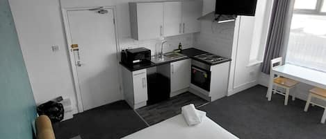 Habitación de hotel con cama, kitchenette, televisor y ventana con cortinas.