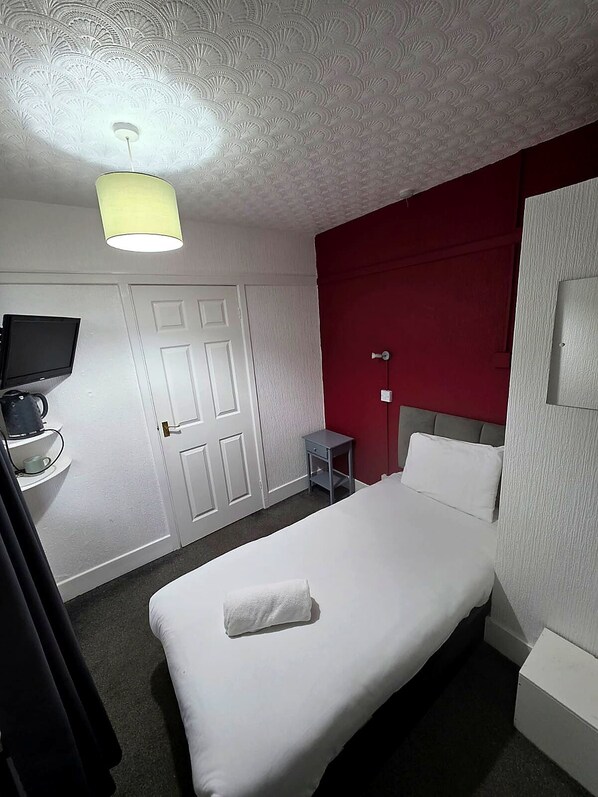 Ein Hotelzimmer mit Bett, Fernseher, kleinem Tisch und einer roten Akzentwand.
