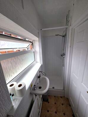 Ein kleines Badezimmer mit Dusche, Waschbecken und Fenster.