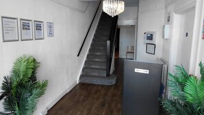 A hotel reception area with a reception desk, a staircase, and potted plants. - Standard Triple Ensuite (Skegness)