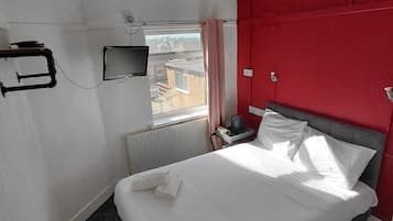 Una camera d'albergo con un letto, una televisione, un termosifone e una finestra con tende.