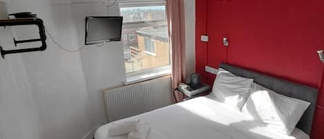 A hotel room with a bed, a television, a radiator, and a window with curtains.