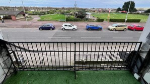 A view from a balcony with a metal railing, overlooking a parking lot with several cars and a green sign in the background. - Standard Triple Ensuite (Skegness)