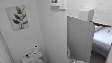 Pieni, käytännöllinen kylpyhuone, jossa on wc, pesuallas ja peili.