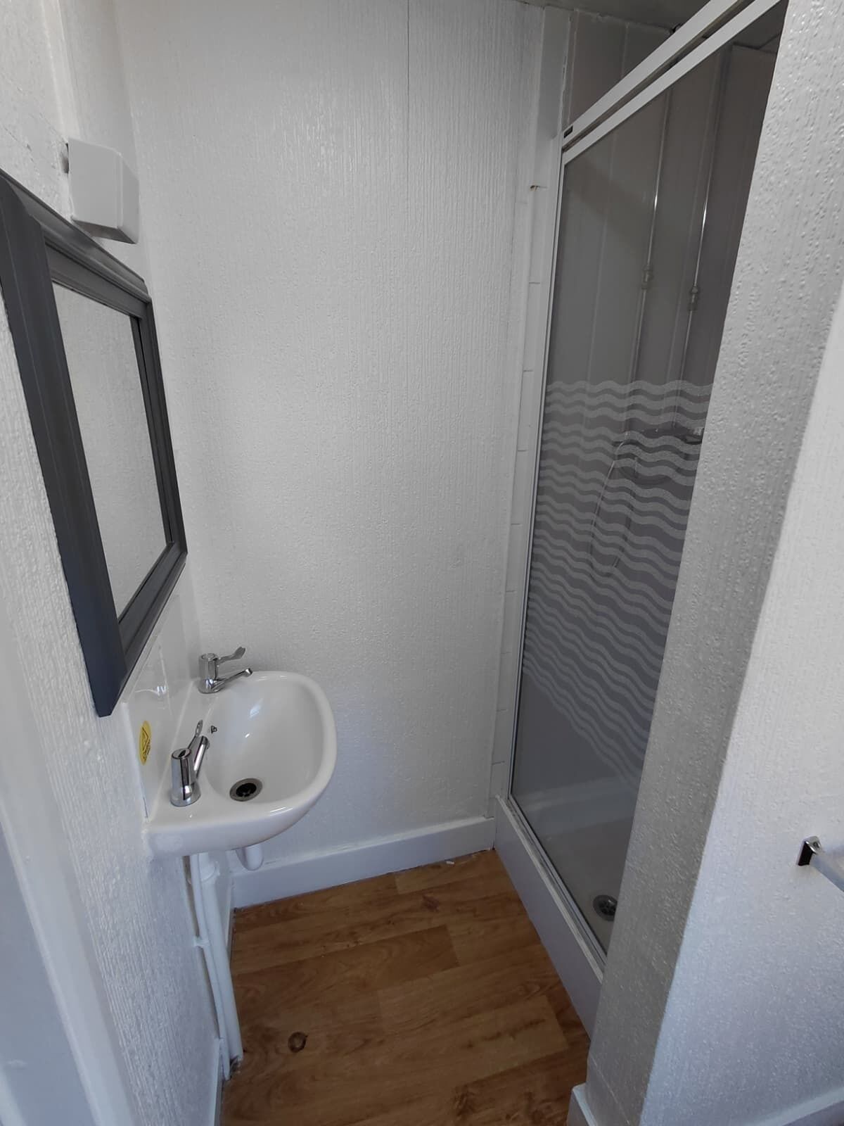 A small bathroom with a white sink, a mirror, and a shower enclosure.