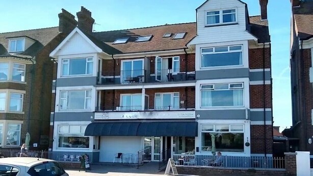 Un immeuble à plusieurs étages, avec un restaurant au rez-de-chaussée et des logements aux étages supérieurs.