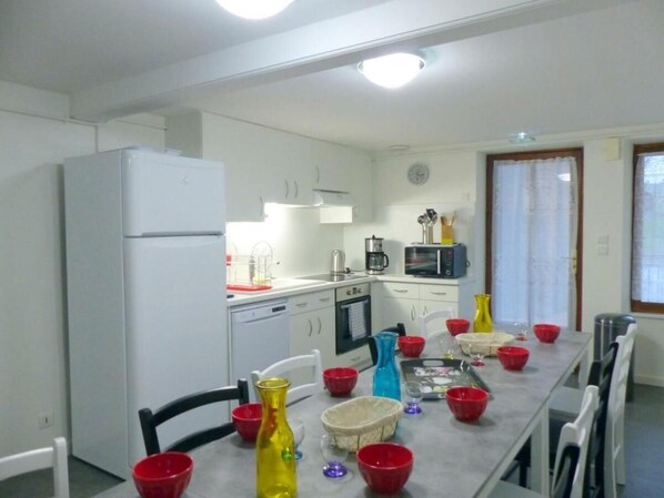Eine Küche mit weißen Schränken, einem Kühlschrank, einer Mikrowelle und einem Esstisch, gedeckt mit roten und gelben Schüsseln.