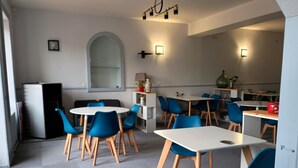 Un comedor moderno con mesas redondas y sillas azules, un refrigerador blanco y un espejo grande en la pared.