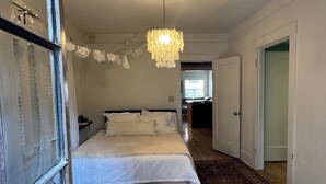 A bedroom with a large bed, a red chair, a wooden floor, and a chandelier. - Charming Historic Downtown Apartment, One Bedroom, with Enclosed Patio (Tucson)