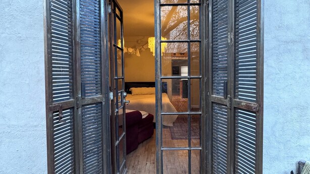 A doorway with open shutters leading to a room with a bed and a sofa. - Charming Historic Downtown Apartment, One Bedroom, with Enclosed Patio (Tucson)
