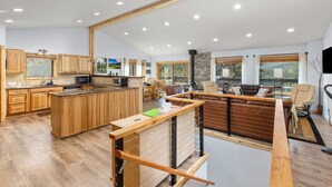 A spacious kitchen with wooden cabinets and a central island, a dining area with a sofa and chairs, and large windows offering views of the outdoors. - Hot Tub - Near Eldora - Views - Pool Table (Rollinsville)