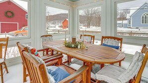 A covered dining area with a wooden table and chairs, large windows, and a view of a red barn and a blue building. - Mtn-View Rupert Village Home on Private Acreage (West Rupert)