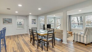 Een ruime woonkamer met een houten eettafel en stoelen, een bank en een gestreept fauteuil.