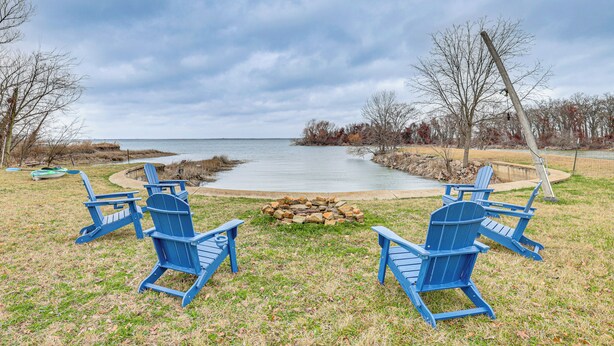 Een landschap aan een meer, met vier blauwe Adirondack-stoelen rond een vuurkuil, met uitzicht op een rustig meer.