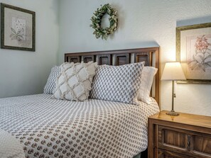 A neatly made bed with patterned bedding, a wooden headboard, a bedside table with a lamp, and a framed floral artwork on the wall. - Spacious Four Bedroom House in South Tulsa w/ Backyard - Close to everything! (Tulsa)