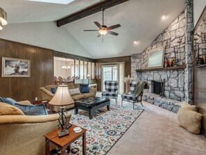 A cozy living room with a stone fireplace, wooden paneling, and a ceiling fan. - Spacious Four Bedroom House in South Tulsa w/ Backyard - Close to everything! (Tulsa)