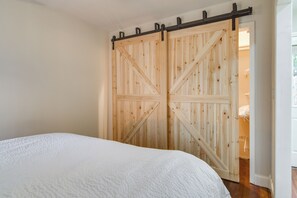 Ein Schlafzimmer mit großem Holzschrank, einem Bett mit weißer, strukturierter Bettdecke und Holzboden.