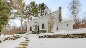 Una casa blanca con un muro de piedra al frente, rodeada de árboles y cubierta de nieve.
