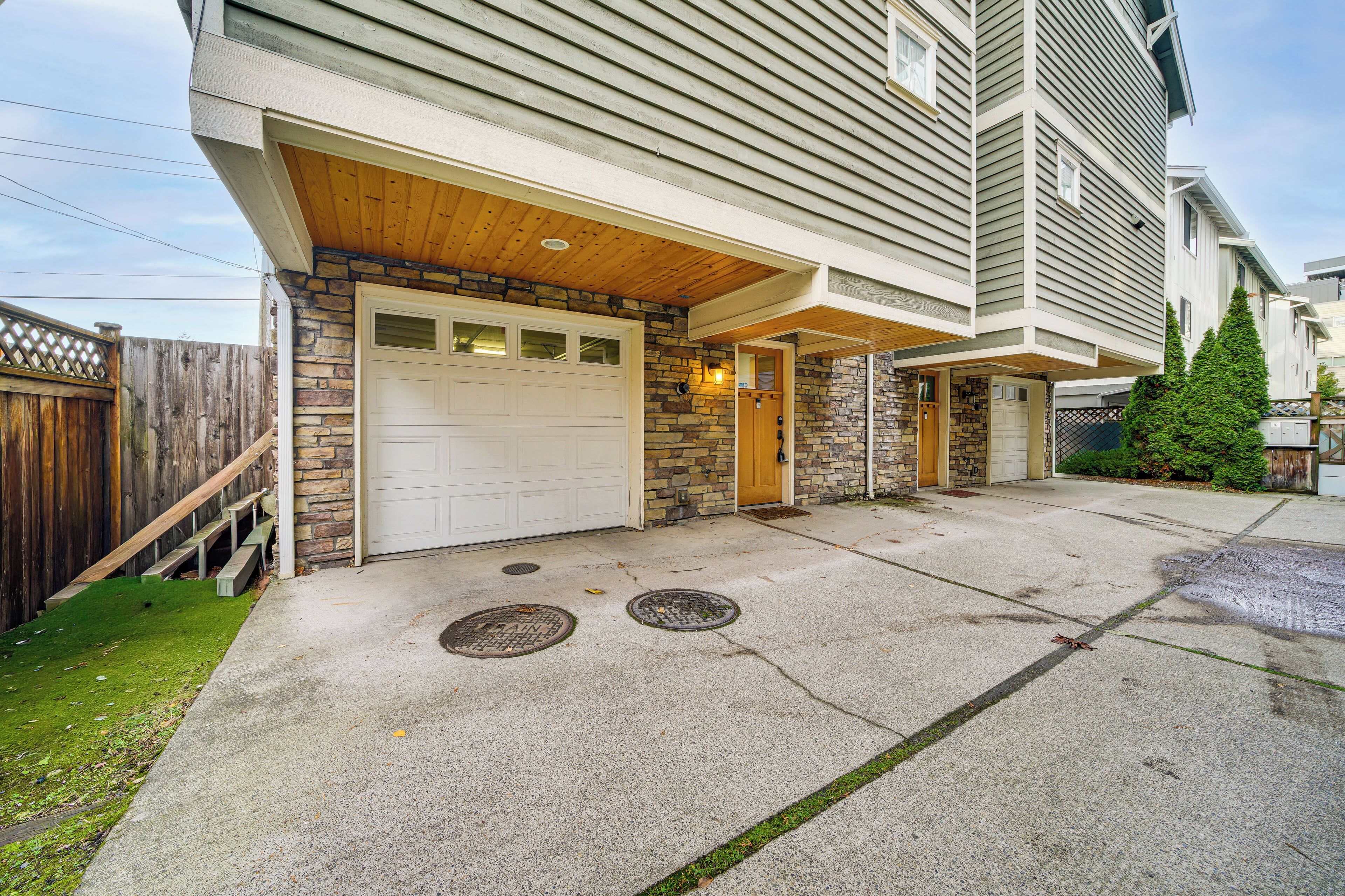 A residential building with a garage, stone facade, and a wooden deck.