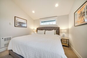 A bedroom with a large bed, a window, a headboard, a nightstand, and a wall-mounted heater.