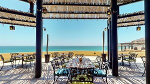 An outdoor dining area with a view of the sea, featuring tables and chairs under a thatched roof. - Oceanfront resort, semi-private beach within walking distance to all amenities (Cabo San Lucas)