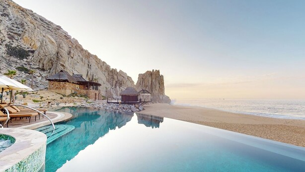 A beachfront infinity pool with a view of the ocean, a rocky cliff, and a small hut structure. - Oceanfront resort, semi-private beach within walking distance to all amenities (Cabo San Lucas)