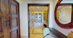 A hallway with a wooden door, a mirror, and a tiled floor leading to a bathroom with a sink and a toilet. - Oceanfront resort, semi-private beach within walking distance to all amenities (Cabo San Lucas)