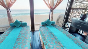 A beachside room with two beds, each with a patterned bedspread and pillows, a wooden floor, and a view of the beach and ocean. - Oceanfront resort, semi-private beach within walking distance to all amenities (Cabo San Lucas)