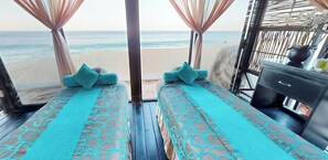 A beachside room with two beds, each with a patterned bedspread and pillows, a wooden floor, and a view of the beach and ocean. - Oceanfront resort, semi-private beach within walking distance to all amenities (Cabo San Lucas)